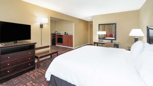 Une chambre d’hôtel avec un grand lit, une télévision, un bureau avec une chaise, une lampe et une salle de bain visible à travers une porte ouverte.