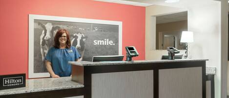 A hotel reception desk with a framed picture of cows and the word "smile." on the wall.