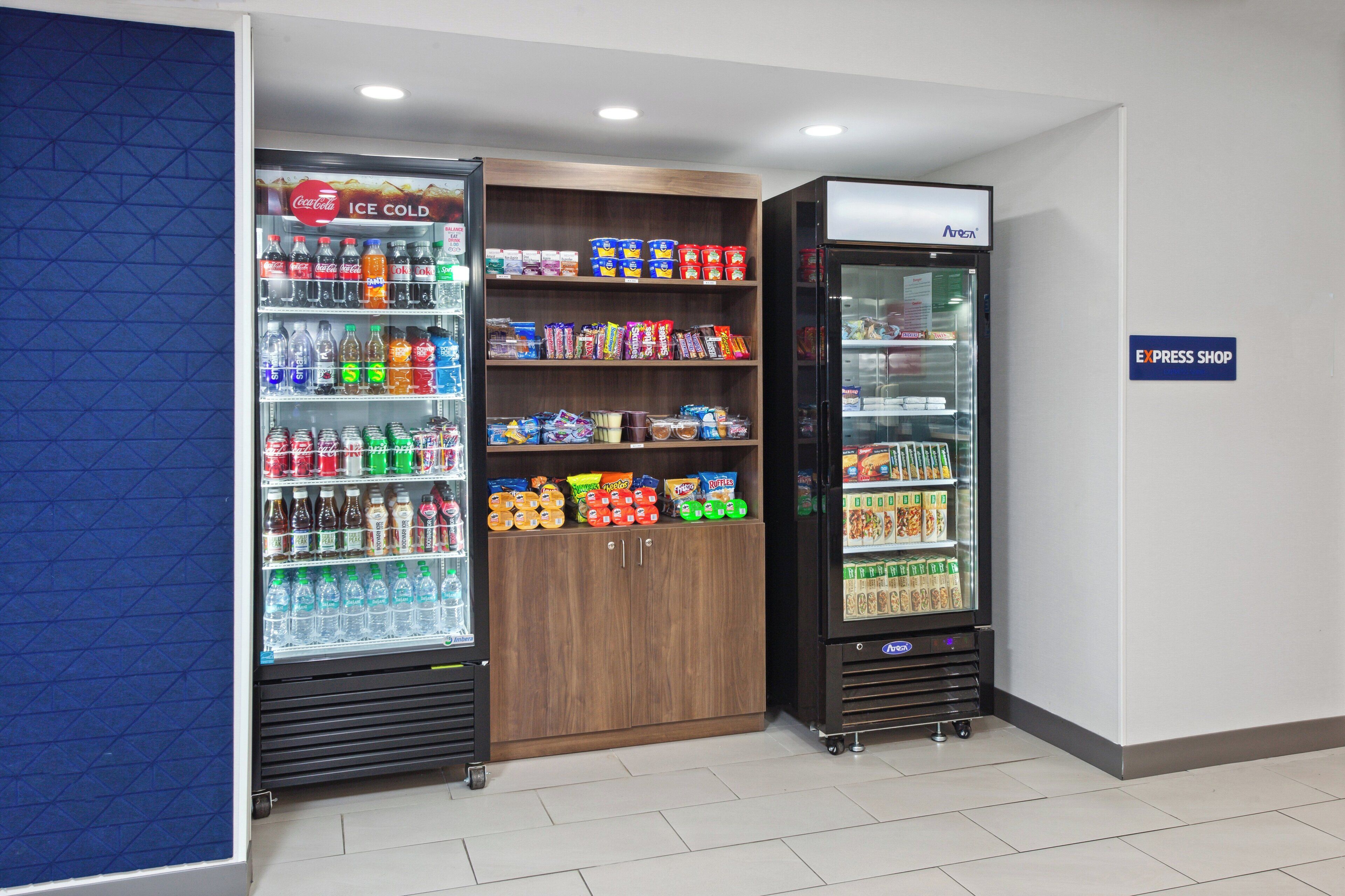 Ein Verkaufsbereich mit verschiedenen Getränke- und Snackoptionen, darunter ein Coca-Cola-Kühler, ein Nutella-Spender und ein Kühlregal mit der Aufschrift "EXPRESS SHOP".