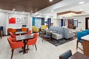 A modern hotel lobby with a mix of seating options including tables and chairs, a refreshment shop, and a map on the wall.