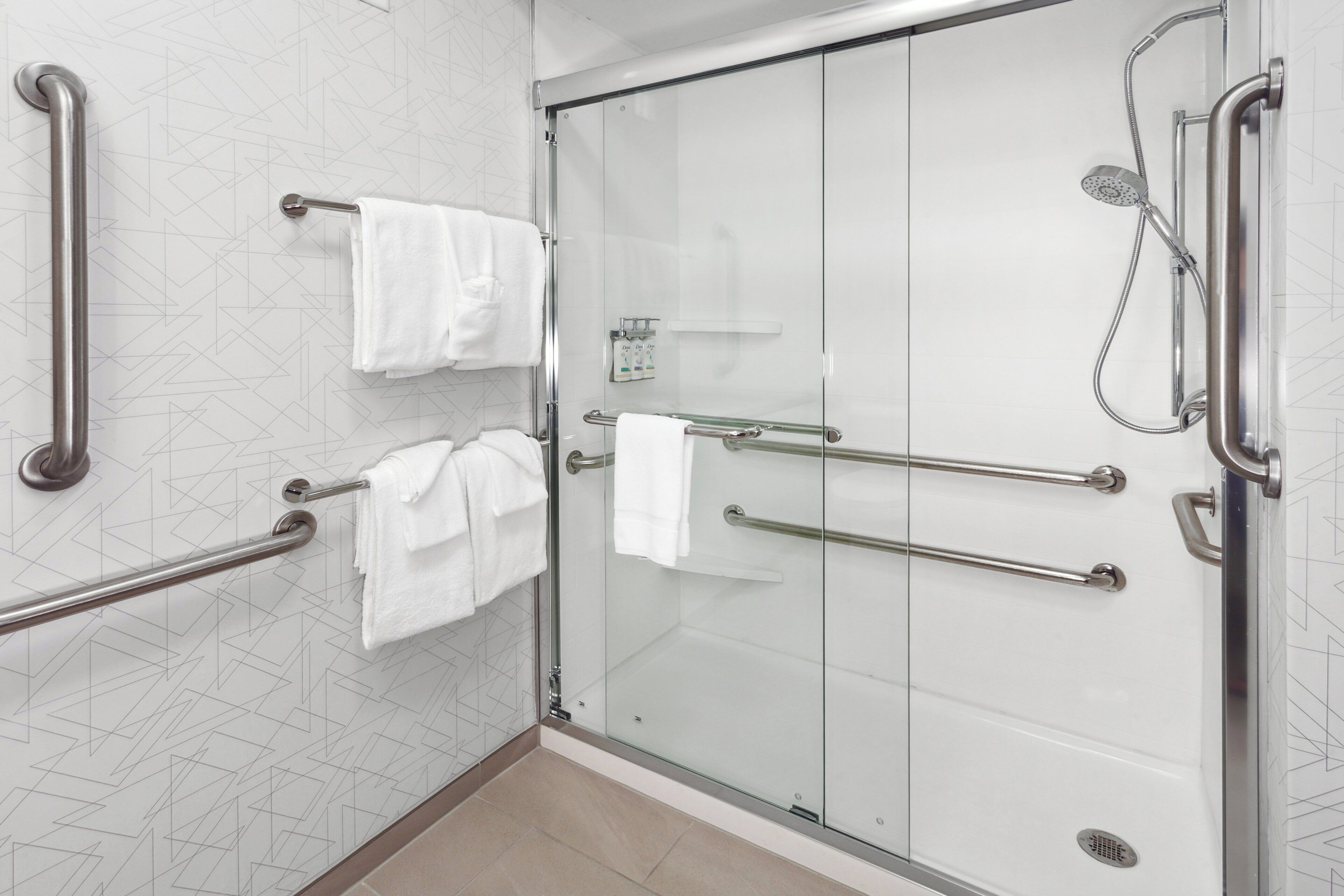 Un baño moderno con cabina de ducha de vidrio, barras de apoyo y panel de control.