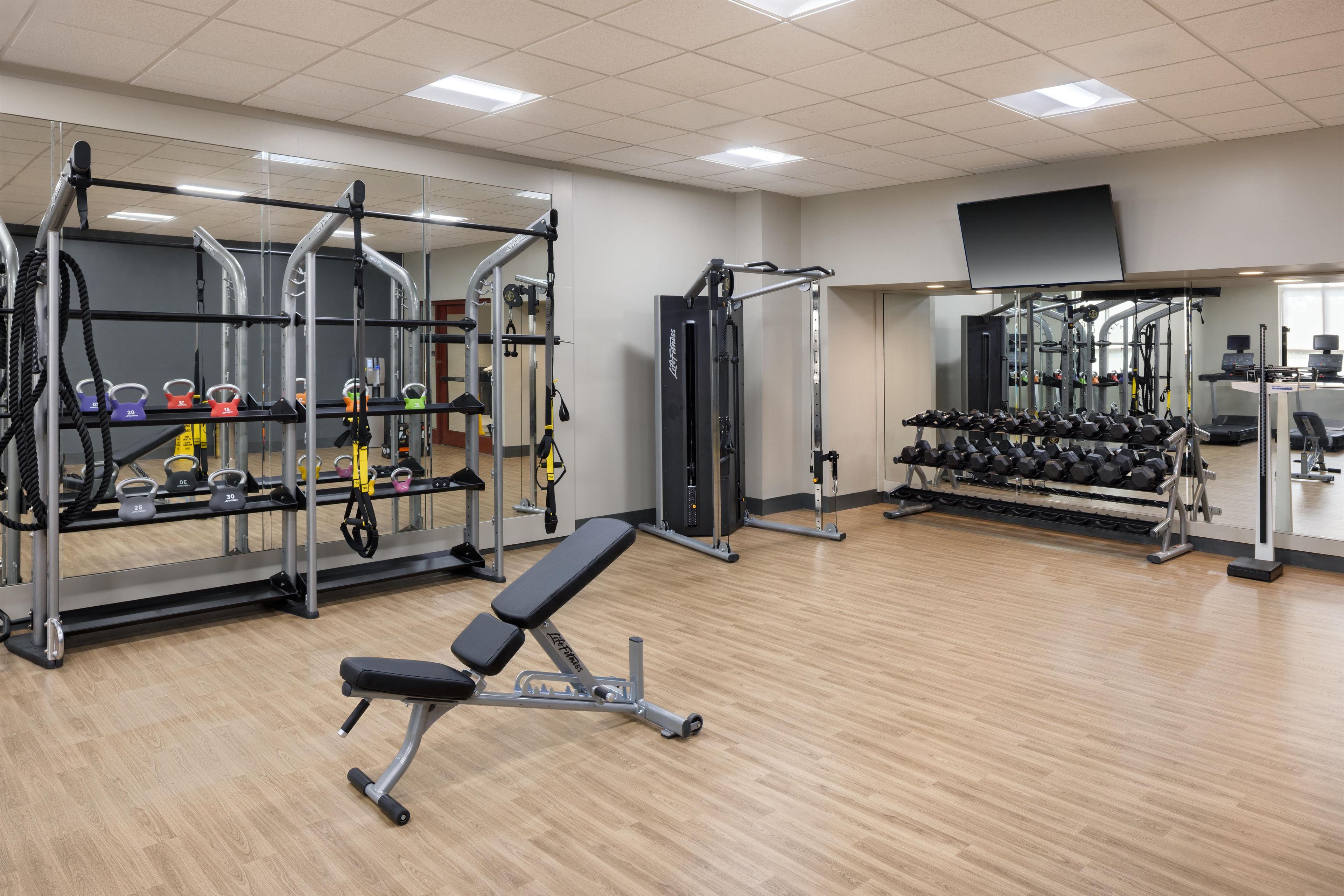 Un gimnasio con diferentes equipos de ejercicio, como bancos, estantes para pesas y mancuernas.
