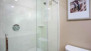 Ducha con mampara de vidrio, cabezal de ducha manual, inodoro y un cuadro en la pared.