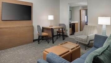 Une chambre d’hôtel équipée d’un téléviseur à écran plat fixé au mur, d’un bureau avec deux chaises, d’un canapé et d’une petite table.