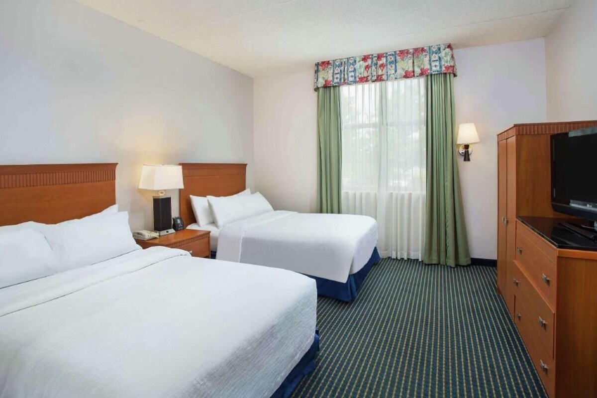 A hotel room with two beds, a TV, a desk with a lamp, and a window with curtains.