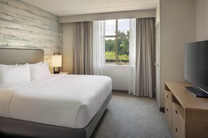 A hotel room with a large bed, a television on a wooden dresser, and a window with curtains. - Embassy Suites by Hilton Lexington/UK Coldstream (Lexington)
