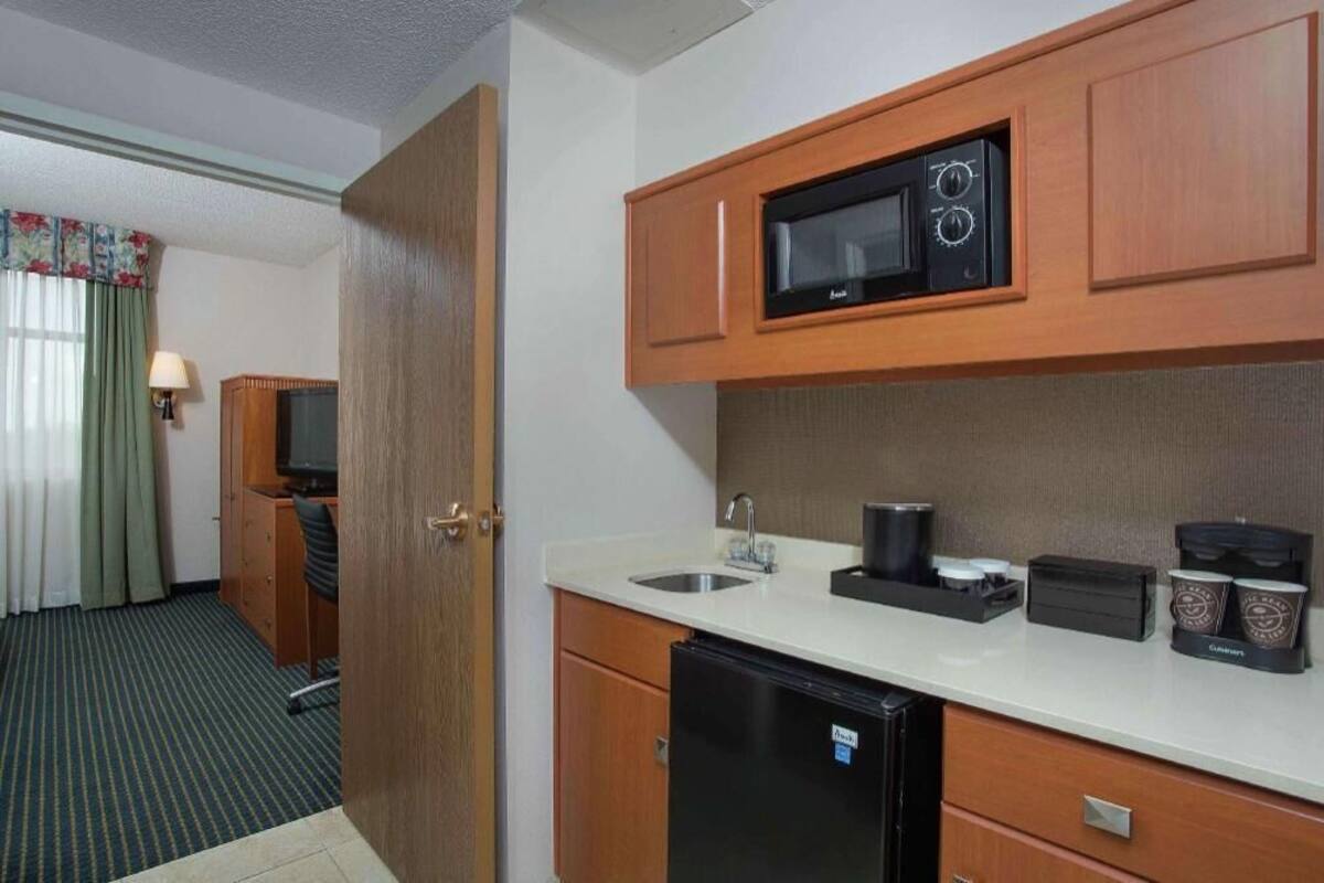 Ein kleines Hotelzimmer mit Kochnische, inklusive Mikrowelle, Spüle und Kühlschrank.