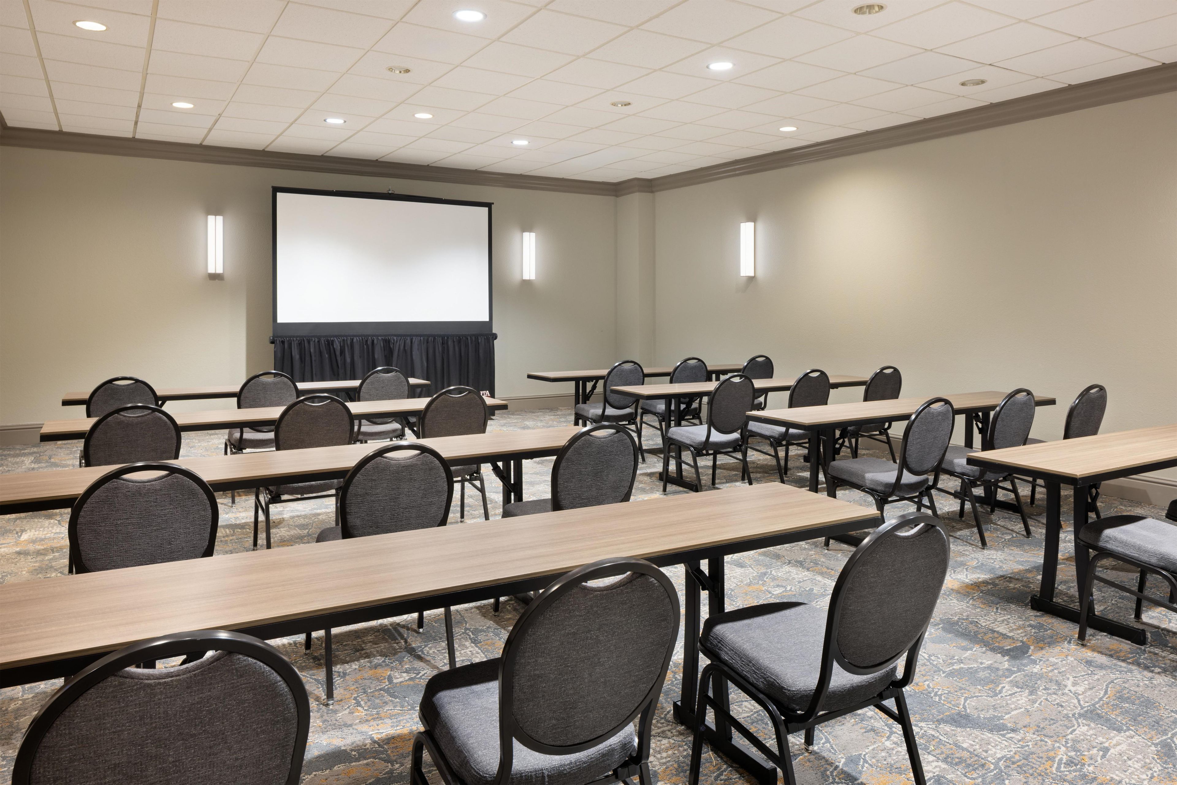 Une salle de conférence équipée de plusieurs tables et chaises, d’un grand écran et d’un projecteur.