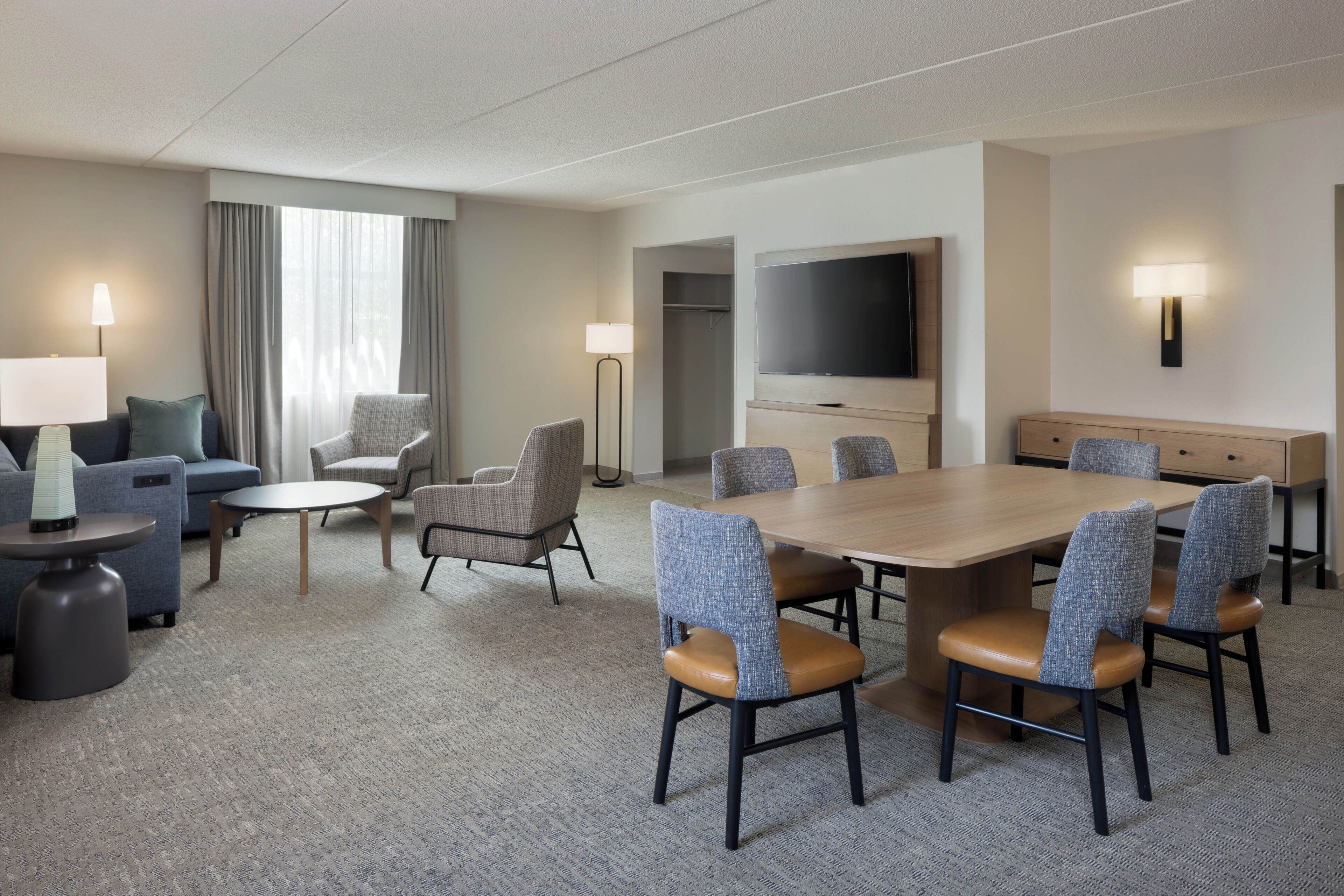 Habitación de hotel con una mesa de comedor, sillas, un sofá, un televisor y una lámpara.