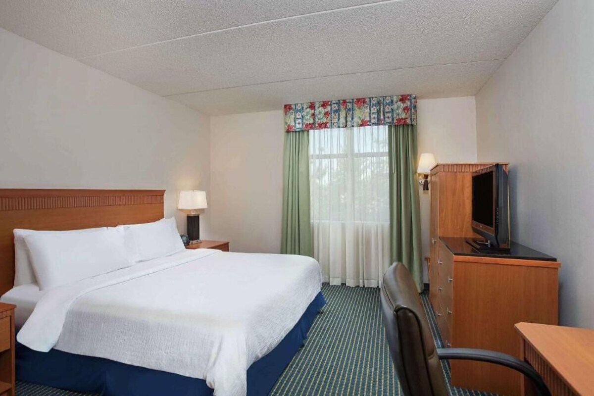 A hotel room with a bed, a desk, a chair, a television, and a window with curtains.