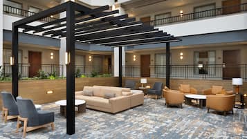 Un vaste hall d’entrée intérieur au design moderne, comprenant un espace salon central avec des canapés et des fauteuils, un mur d’accent en bois et une mezzanine avec des balcons.