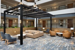 Eine großzügige, innenliegende Lobby mit modernem Design, ausgestattet mit einer zentralen Sitzecke mit Sofas und Sesseln, einer Wand als Holz-Akzent und einer Zwischenebene mit Balkonen.
