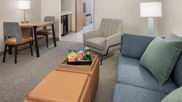 A hotel room with a dining area, a sofa, a chair, and a small table with snacks.