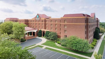 A large brick building with a red roof, labeled 'Embassy Suites by Hilton,' featuring a spacious parking lot and well-maintained landscaping.