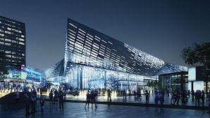 En moderne bygning med et unikt, kantet design, store glasfacader og en rummelig plads med forsamlede mennesker.