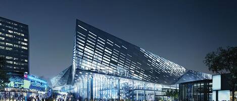 A modern building with a unique angular design, large glass windows, and a spacious plaza with people gathered around.