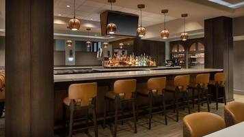 A bar area with a long counter, multiple bar stools, and a variety of bottles and glasses.