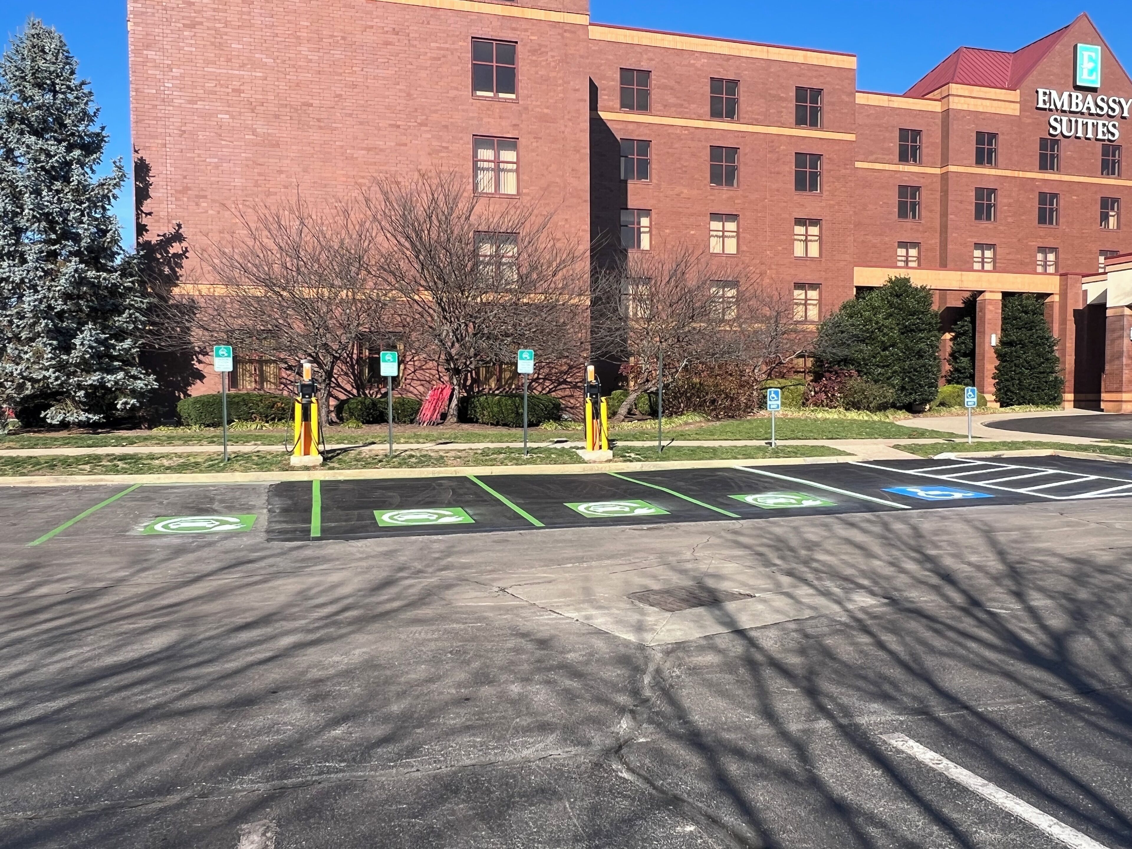 A parking lot with designated spaces for electric vehicles and handicapped parking, in front of a building labeled "Embassy Suites."
