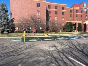 Un estacionamiento con espacios reservados para vehículos eléctricos y estacionamiento para discapacitados, frente a un edificio con el rótulo "Embassy Suites".