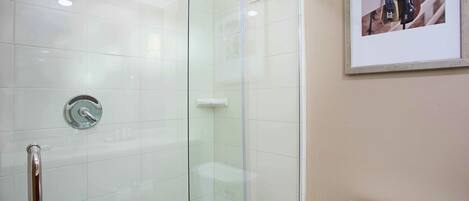 A glass-enclosed shower with a handheld showerhead, a toilet, and a framed picture on the wall.