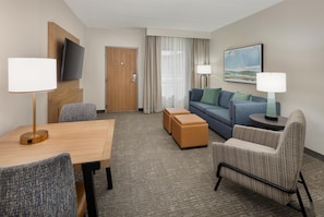 A hotel room with a wooden table, two armchairs, a sofa, a TV mounted on the wall, a painting, and a door. - Embassy Suites by Hilton Lexington/UK Coldstream (Lexington)