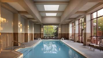A swimming pool with a clear view of the outdoors, surrounded by seating areas and a high ceiling with skylights.