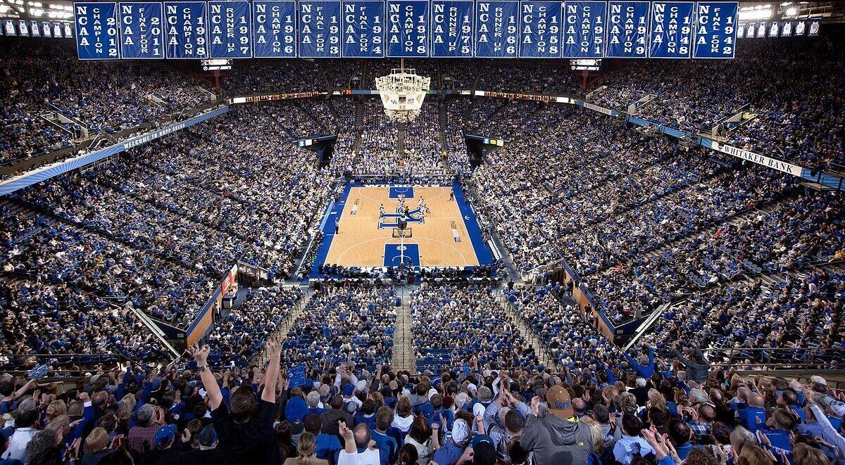 Una cancha de baloncesto rodeada por un estadio grande y abarrotado con asientos azules.