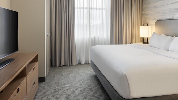 Et hotelværelse med seng, fjernsyn, skrivebord og lampe.