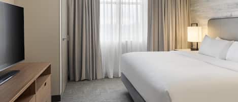Et hotelværelse med seng, fjernsyn, skrivebord og lampe.