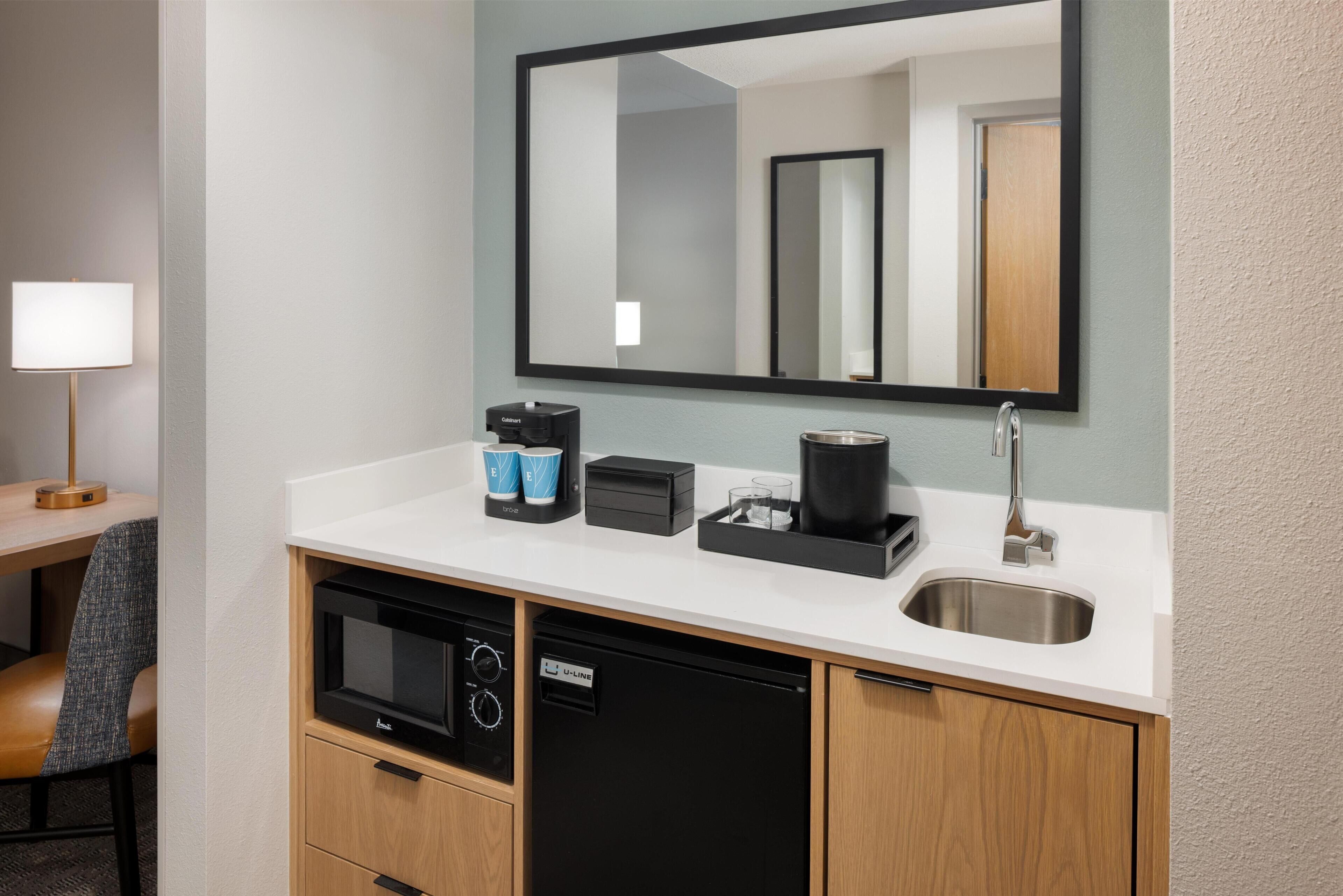 Un baño moderno con un espejo grande, un lavabo, una cafetera y un microondas.