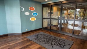 A hotel entrance with a wooden floor, a doormat with the text "MAKING YOU HAPPY," and hexagonal signs on the wall with words "enter," "happy," and "zone." - Hampton Inn Somerset (Somerset)