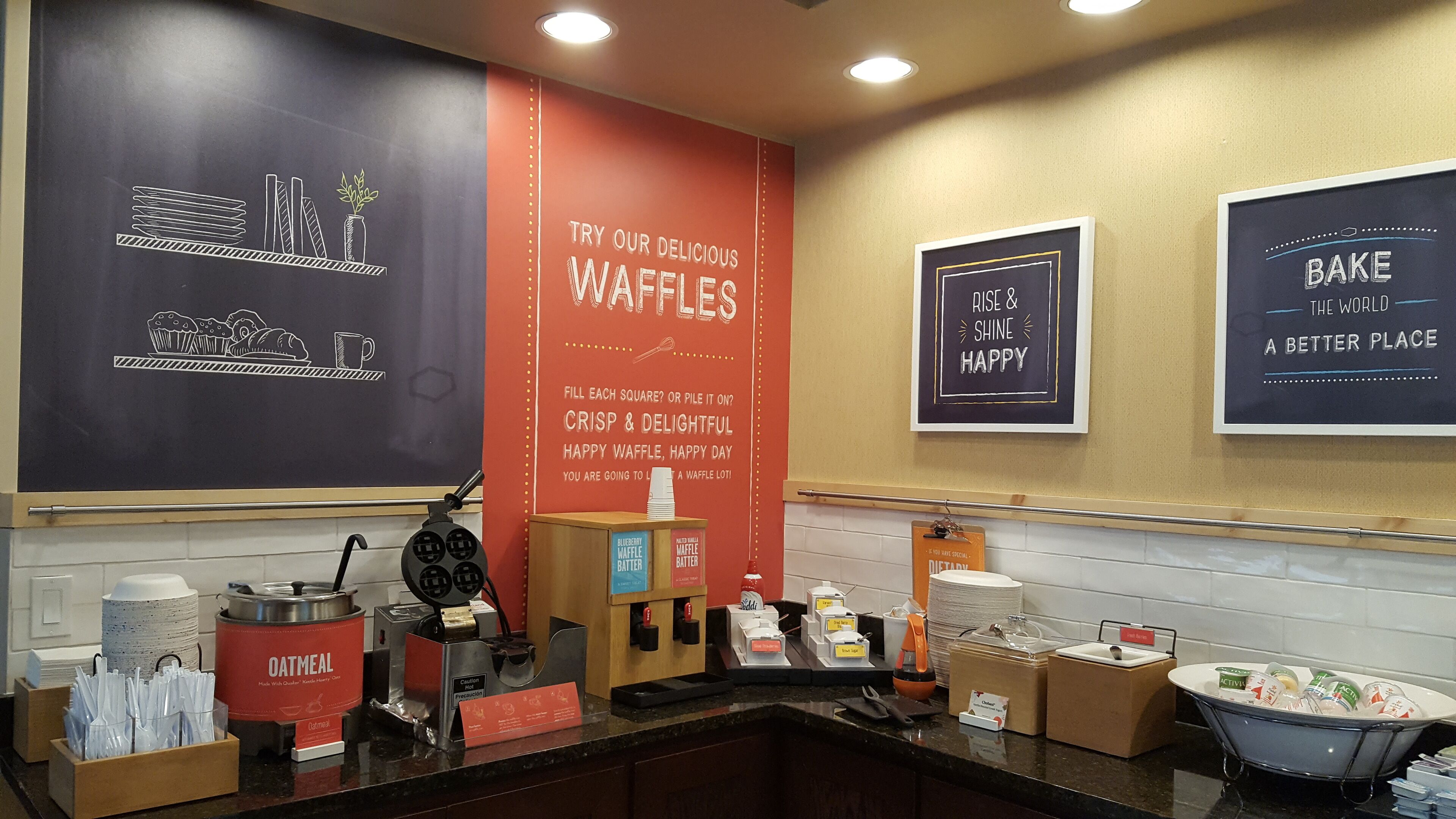 A breakfast station with waffle options, a waffle maker, and a sign promoting waffles.
