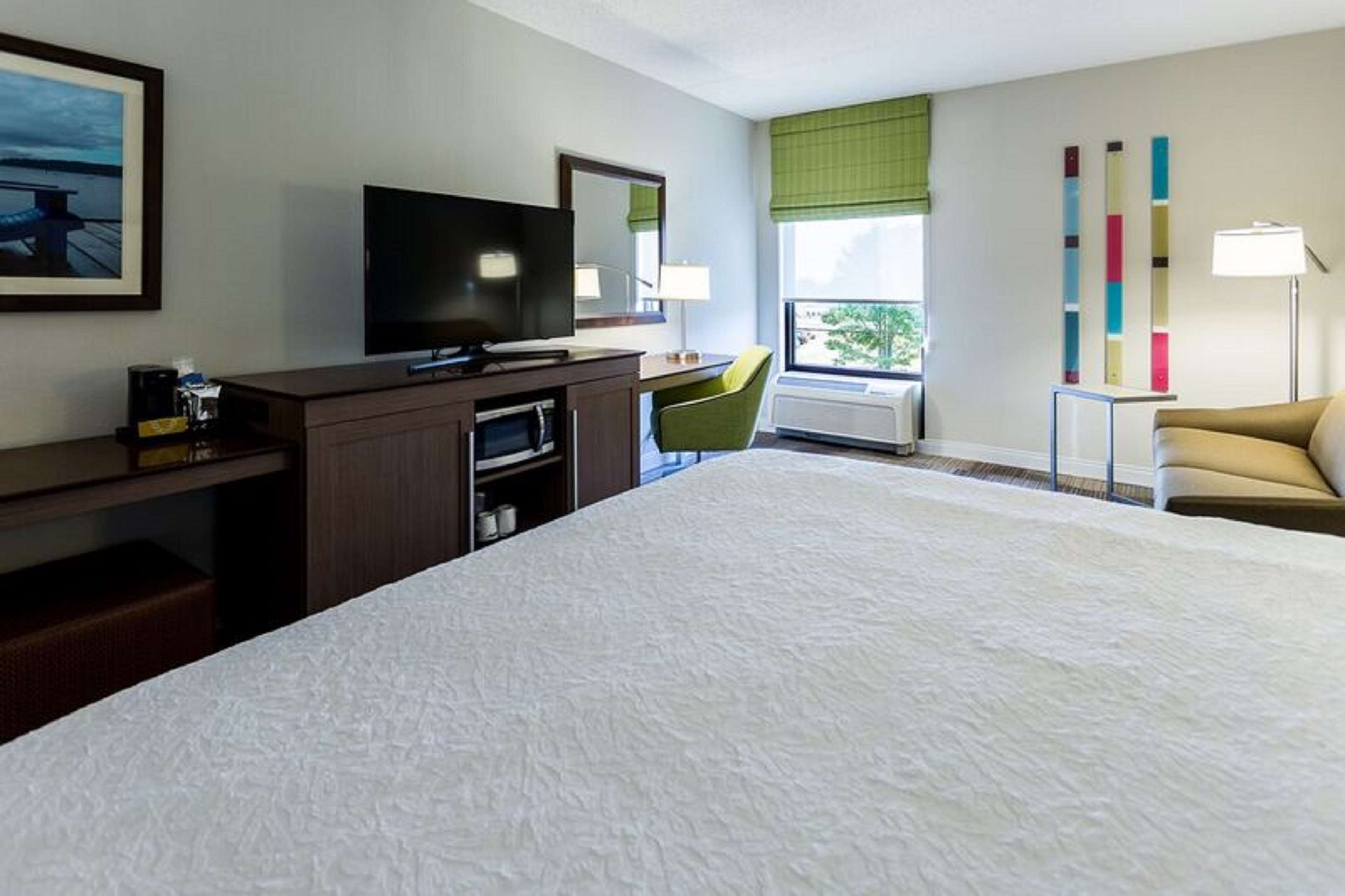Habitación de hotel con una cama grande, un escritorio con televisor de pantalla plana, una silla, una ventana con vistas y una lámpara.