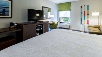 Habitación de hotel con una cama grande, un escritorio con televisor de pantalla plana, una silla, una ventana con vistas y una lámpara.