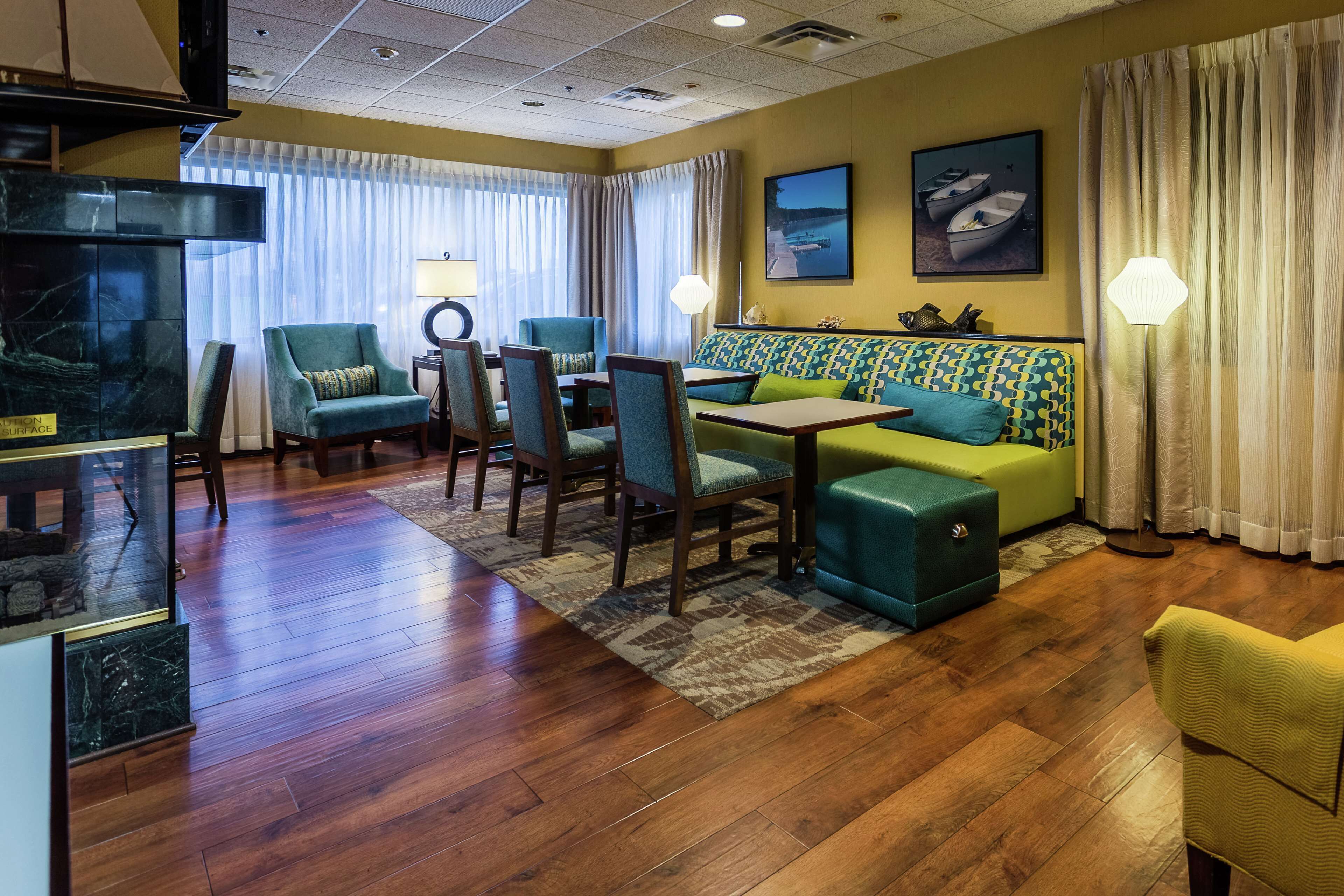 A hotel room with a wooden floor, a sofa, a dining table with chairs, a TV, and a window with curtains.