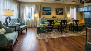 A hotel room with a wooden floor, green upholstered sofas, a patterned rug, and a dining area with chairs and a table. - Hampton Inn Somerset (Somerset)