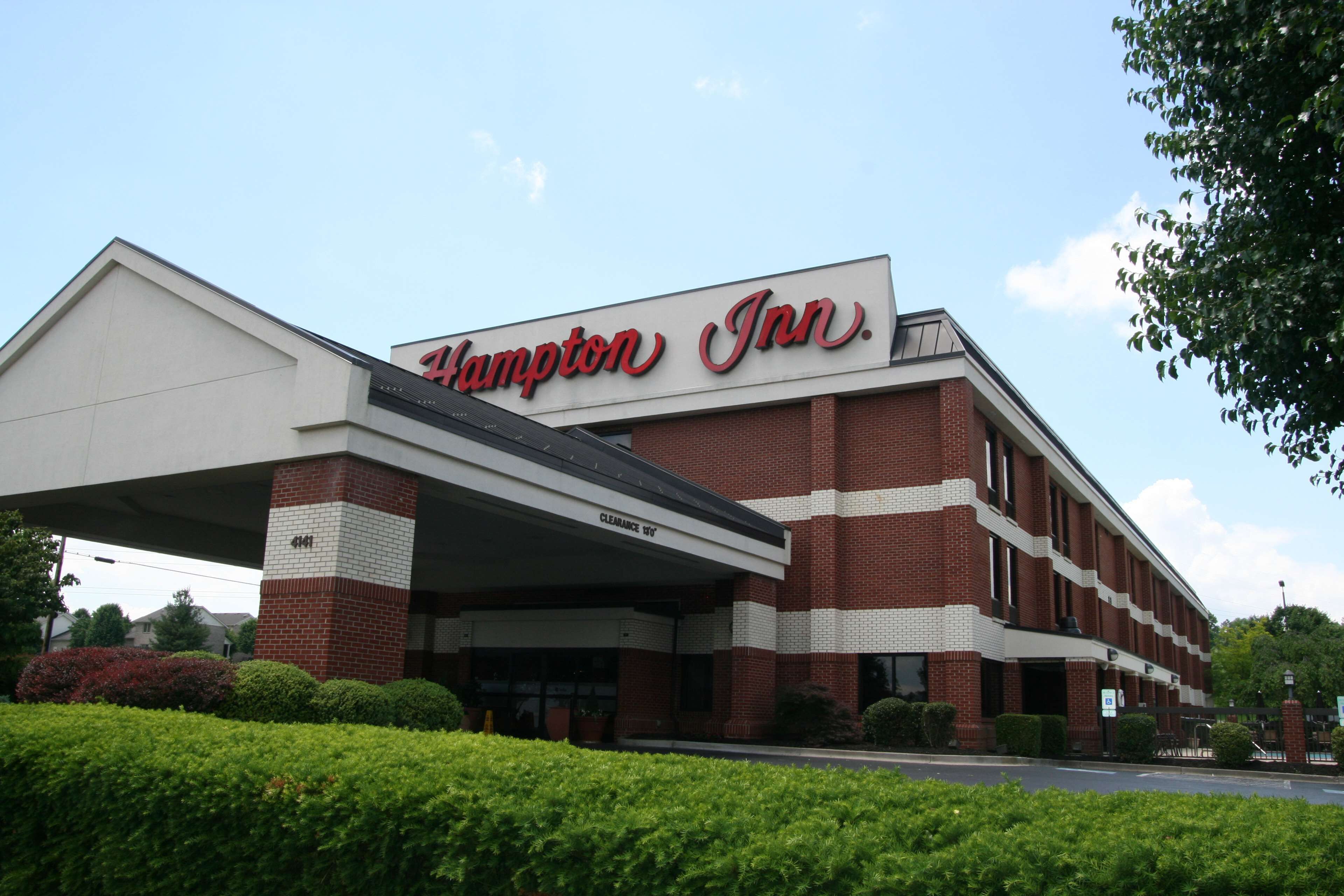 A Hampton Inn building with a prominent sign, a covered parking area, and well-maintained landscaping.