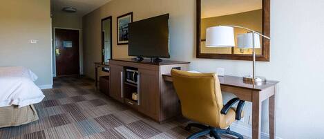 Een hotelkamer met een bed, een bureau met een computer, een stoel, een televisie en een spiegel.