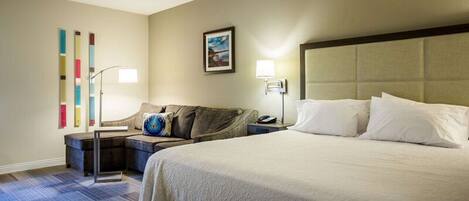 A hotel room with a large bed, a sofa, a nightstand, and a wall-mounted lamp.