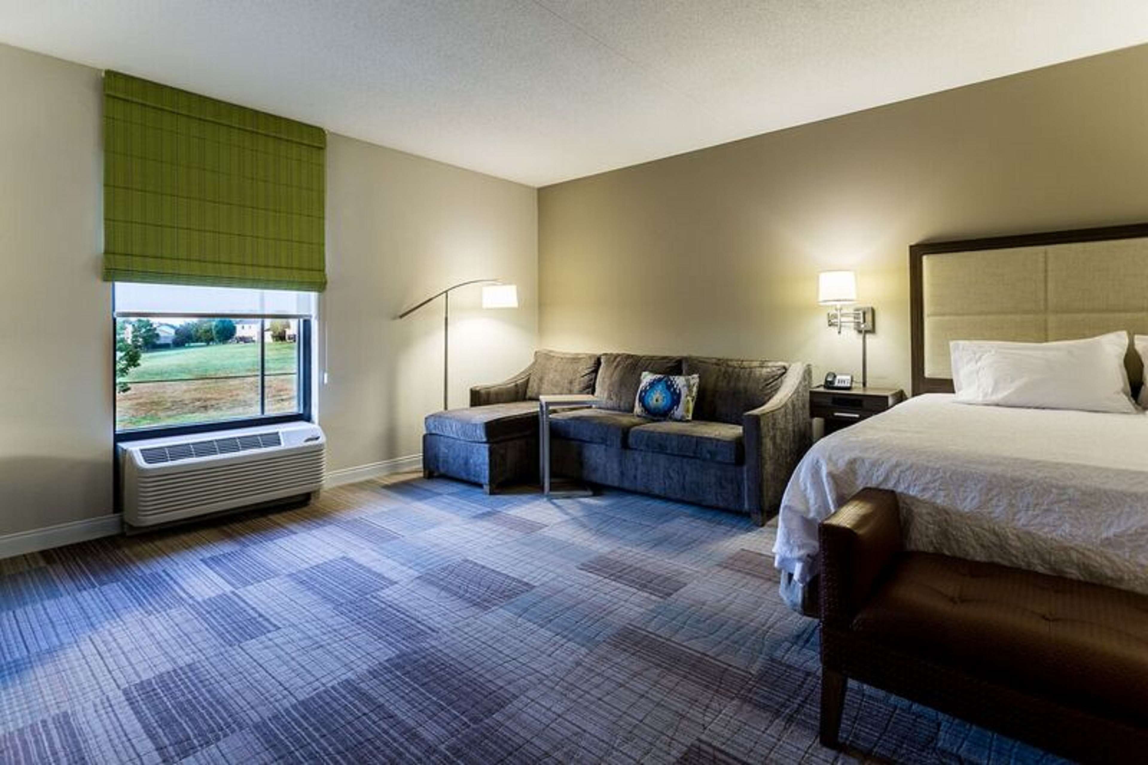 Une chambre d’hôtel avec un grand lit, un canapé, une petite table et une fenêtre donnant sur un paysage verdoyant.