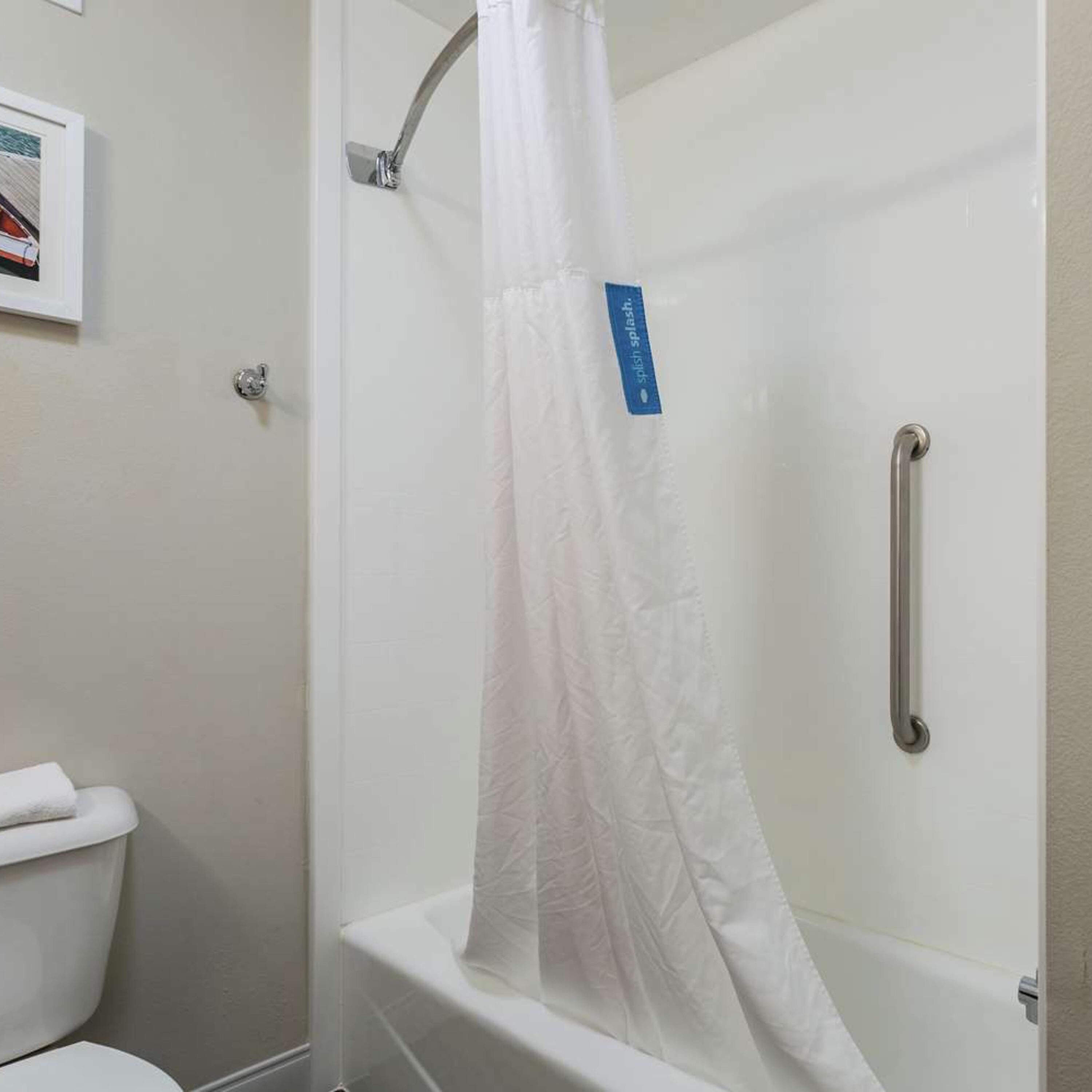 A bathroom with a white shower curtain, a white toilet, and a white bathtub.