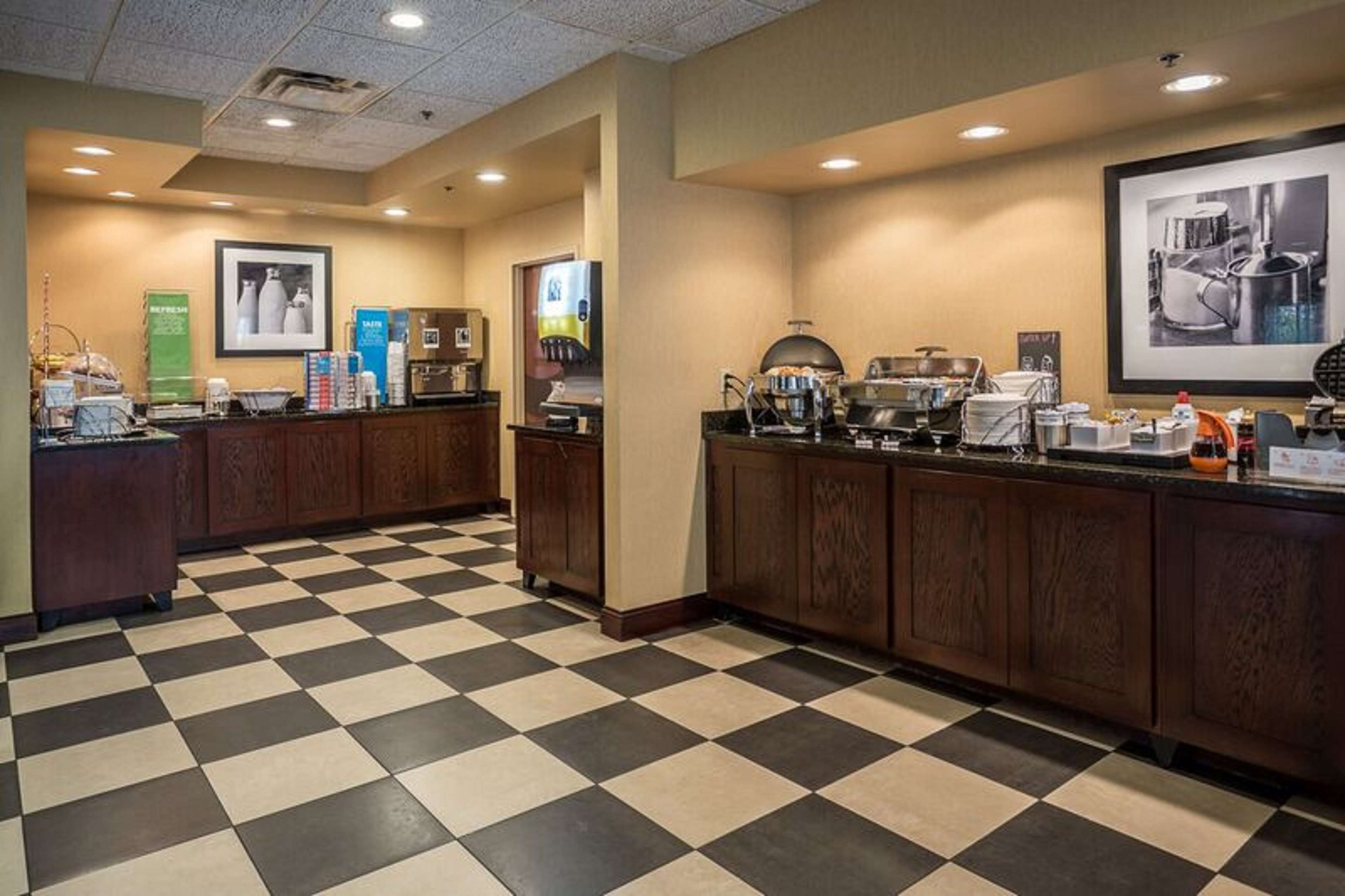 A hotel kitchen with checkered flooring, wooden cabinets, and various kitchen appliances.