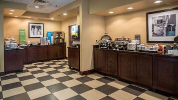 A hotel kitchen with checkered flooring, wooden cabinets, and various kitchen appliances.