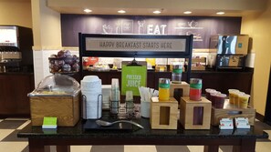 A breakfast buffet with various food and drink options, including fresh-sliced fruit, pressed juice, and yogurt parfaits.
