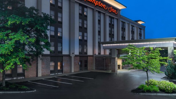 A Hampton Inn hotel building with a modern facade, large windows, and a welcoming entrance.