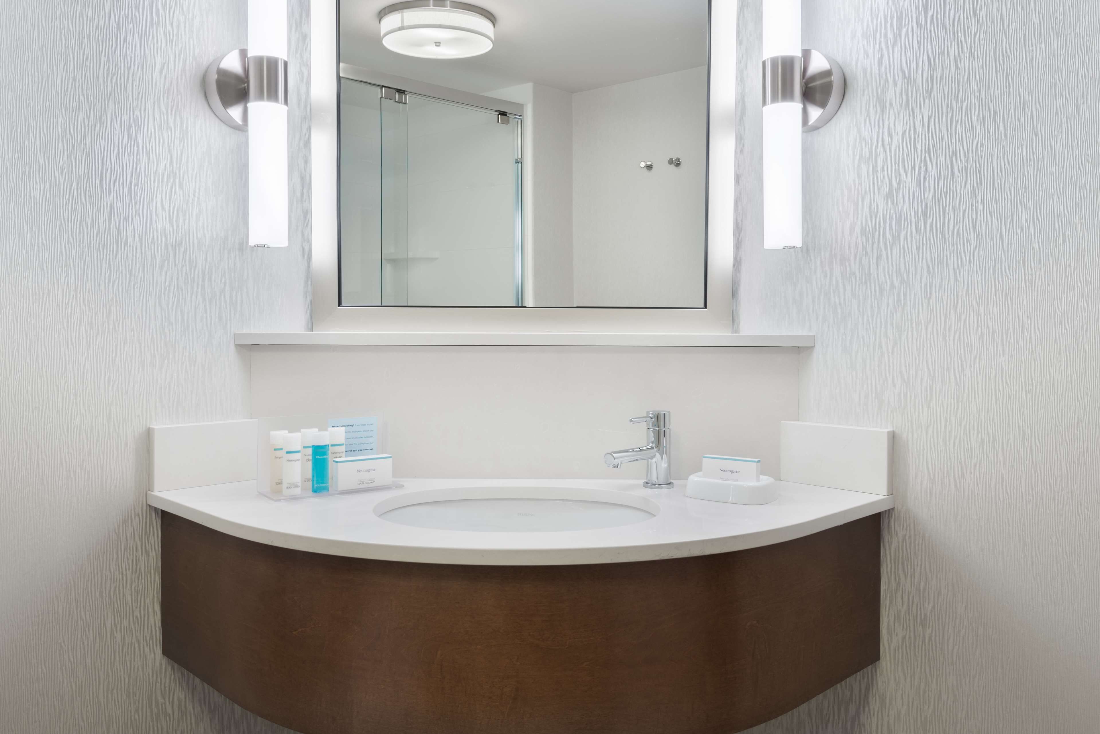 Un baño moderno con un lavamanos blanco, un espejo y dos luces empotradas.