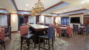 A hotel dining area with a large rectangular table surrounded by chairs, a patterned rug, and a modern chandelier. - Hampton Inn Boston/Marlborough (Marlborough)