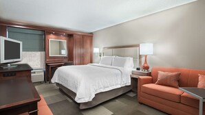 A hotel room with a bed, a desk, a television, a sofa, and a nightstand with a lamp.