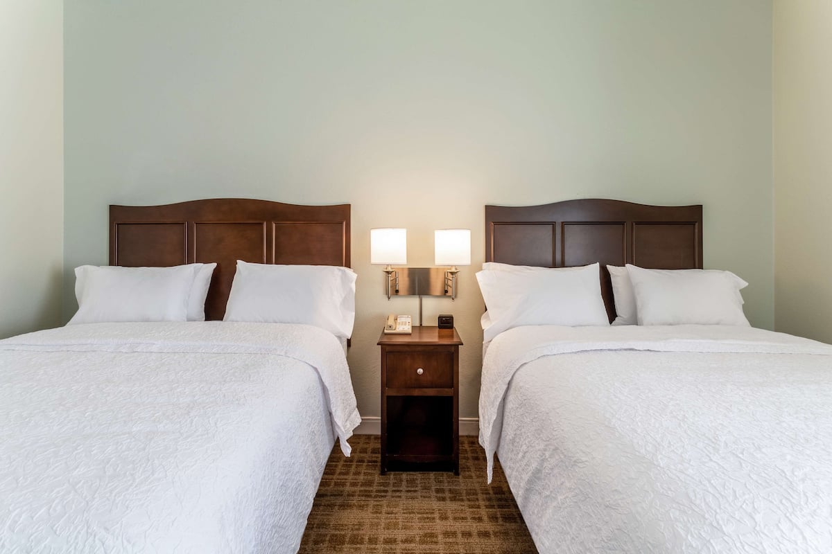 A hotel room with two beds, a nightstand with lamps, and a carpeted floor.