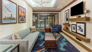 A hotel lobby with a sofa, ottoman, and armchair, a television, and framed pictures on the walls. - Hampton Inn Boston/Peabody (Peabody)
